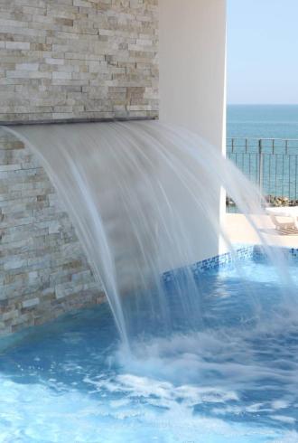 Pool mit Wasserfall und Meerblick, weiße Liegen.